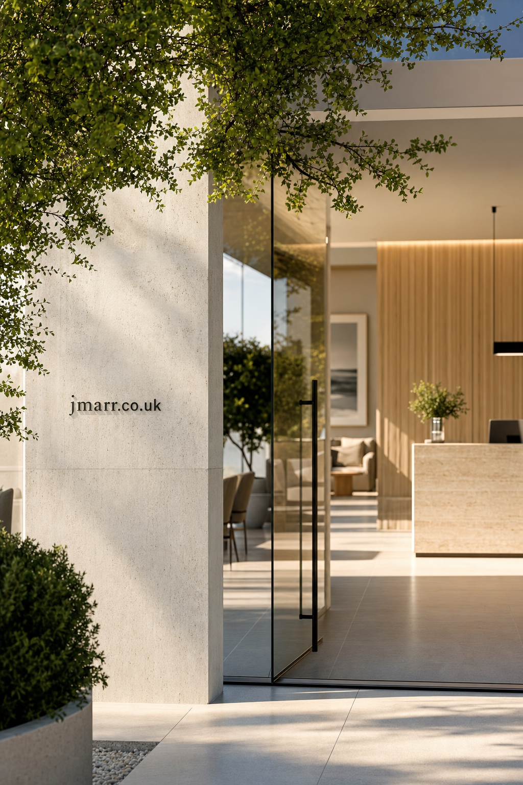 Entrance to a modern office lobby with glass doors, natural stone walls, and greenery, displaying jmarr.co.uk sign on the exterior wall