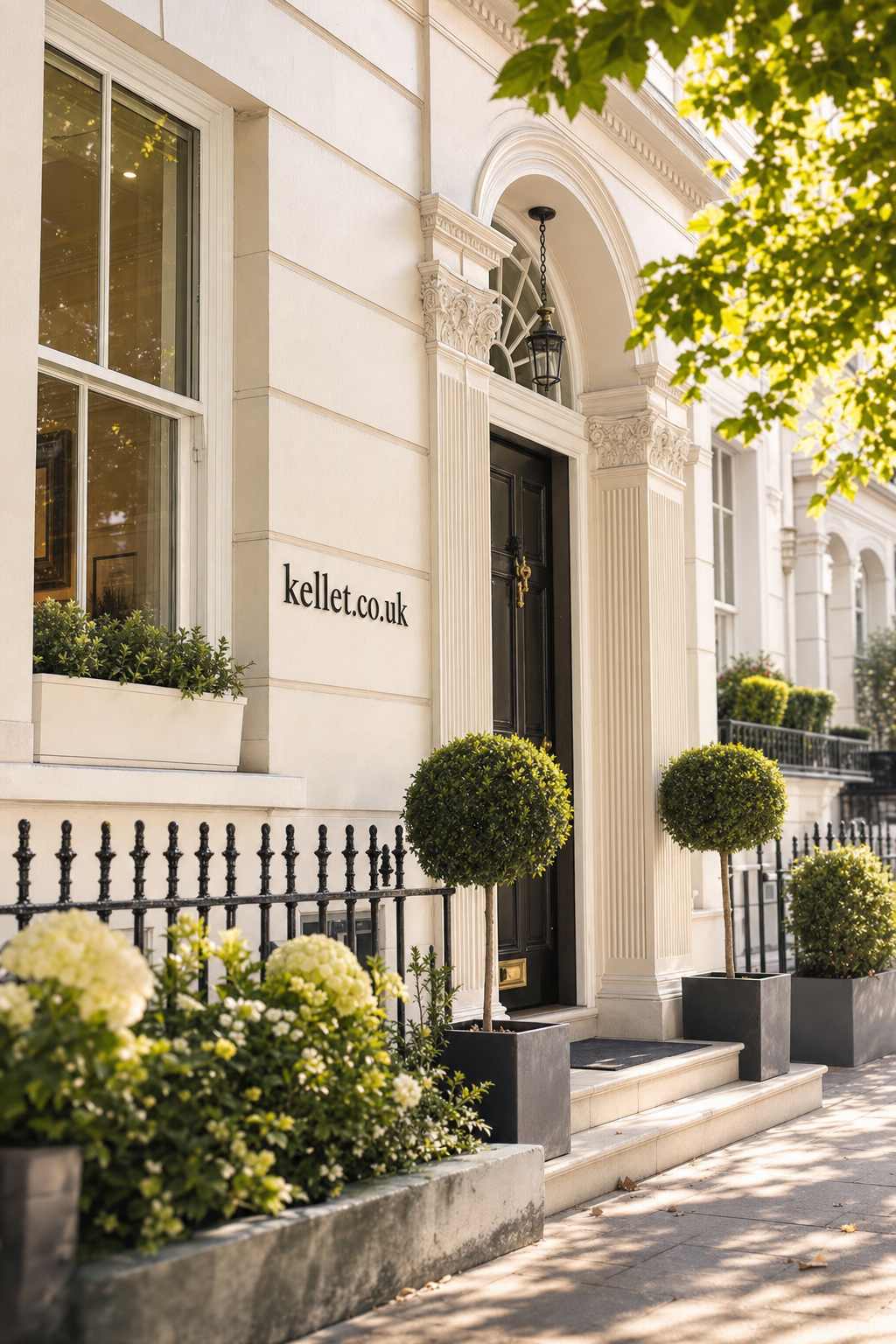 Elegant Georgian townhouse entrance with black door, white columns, green topiary in pots, and plants in front garden under dappled sunlight