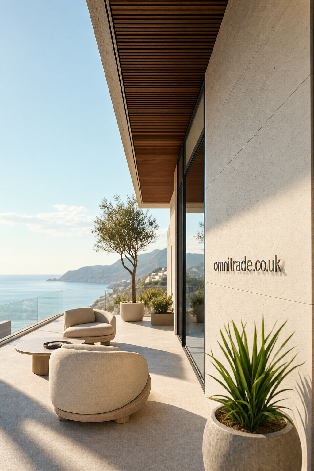 Modern outdoor terrace with comfortable rounded chairs, a low table, potted green plants, overlooking a coastal landscape with mountains and ocean under clear sky, signage on wall reading omnitrade.co.uk